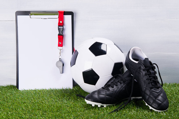 soccer ball, boots and whistle on a tablet for writing, for a judge, lie on the grass, on a gray background - Foto, Imagem