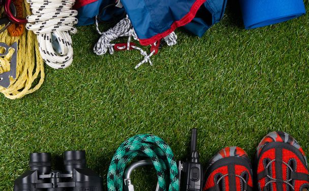 tourist background. on the green lawn are items for travel, shoes, binoculars, a tent for the night with a rug. - Foto, Imagem