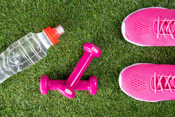 pink sneakers, dumbbells for fitness and a bottle of water, against the background of grass - Foto, Bild