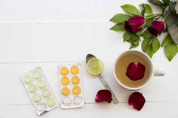 bylinné zdravotní péče hot mix med citron a kašel v krku pastilek pilulky s listy květin na pozadí bílé dřevěné - Fotografie, Obrázek