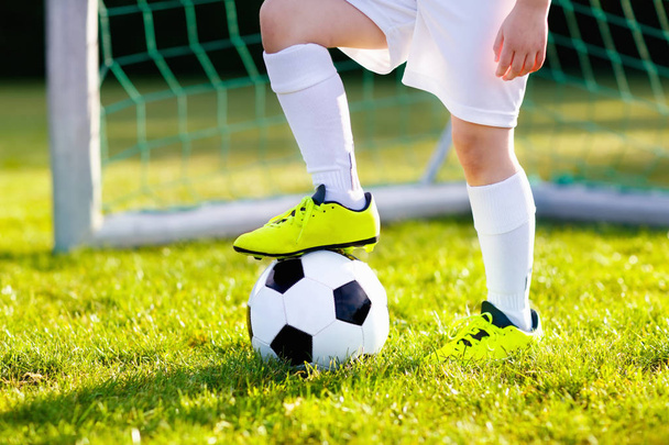Τα παιδιά παίζουν ποδόσφαιρο σε υπαίθριο γήπεδο. Τα παιδιά σκοράρουν ένα γκολ κατά τη διάρκεια του αγώνα ποδοσφαίρου. Μικρό αγόρι κλωτσάει μπάλα. Τρεχούμενο παιδί με φανέλα και αθλητικά παπούτσια. Σχολική ποδοσφαιρική ομάδα. Αθλητική προπόνηση για νέους παίκτες. - Φωτογραφία, εικόνα