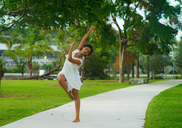 A beautiful African-looking girl with black short hair in a dancing pose dressed in a white dress - Foto, afbeelding