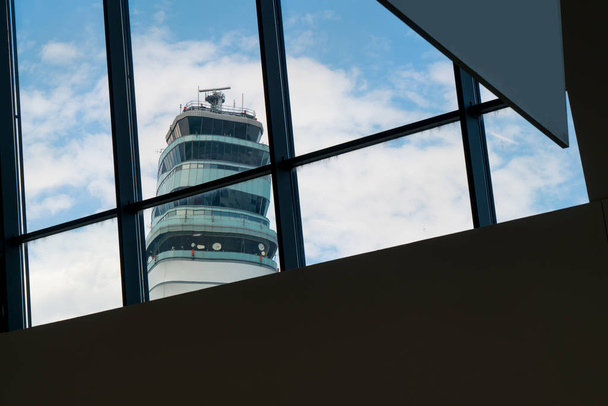 A reptéri terminál épülete kinézett az ablakon. Reptéri forgalomirányító torony sziluett és gyönyörű kék ég antennával és radarral. - Fotó, kép