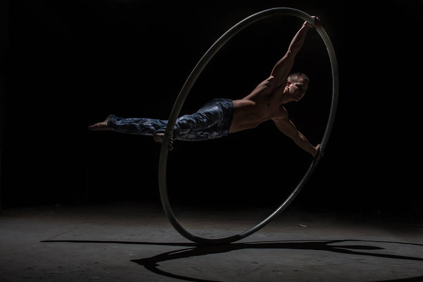 Muscular circus artist in a Cyr Wheel on a black background - Фото, зображення