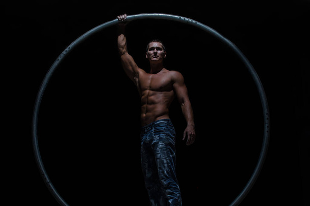 Muscular circus artist in a Cyr Wheel on a black background - Photo, image