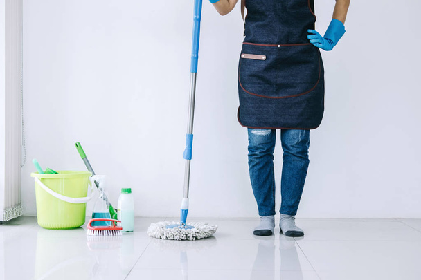 Koncept úklidu a úklidu, Šťastná mladá žena v modrých gumových rukavicích otírání prachu pomocí mop při úklidu na podlaze doma. - Fotografie, Obrázek