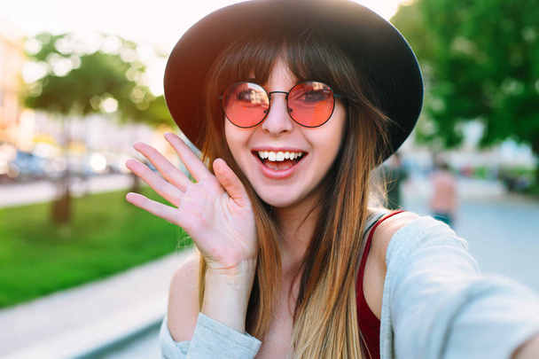 Young smiling teen happy woman making selfie on the street Smiling girl talking on video chat mobile phone app or taking selfie photo for social media. Carefree and happy, sunny spring mood.  - Foto, afbeelding