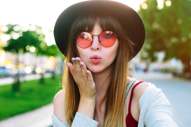 Outdoor portrait of pretty student girl taking a selfie.Beautiful urban woman taking picture of herself, selfie. Filtered image.Pretty hipster girl taking selfie and making duck face. Sending kisses - Photo, image