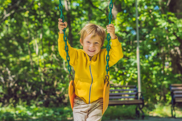Boy in a yellow sweatshirt sits on a swing on a playground in autumn. - Foto, Imagen