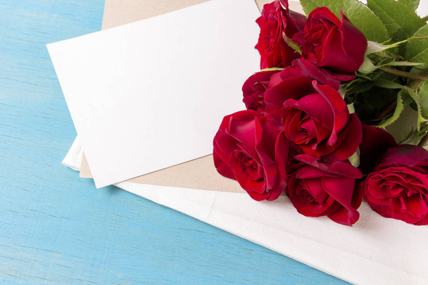 Bouquet of red roses, clean sheet, blue wood background. Copy space. Romantic gift for Valentine's Day holiday. - Photo, Image