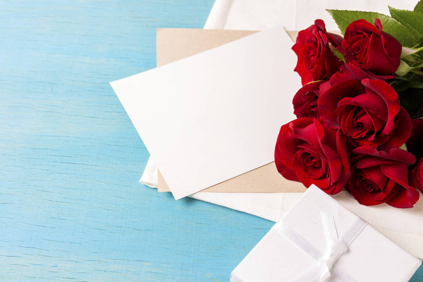 Bouquet of red roses White gift box clean sheet, blue wood background. Copy space. Romantic gift for Valentine's Day holiday. - Foto, afbeelding