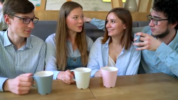 Jóvenes amigos se sientan en un café, beben café y se divierten comunicándose
 - Imágenes, Vídeo