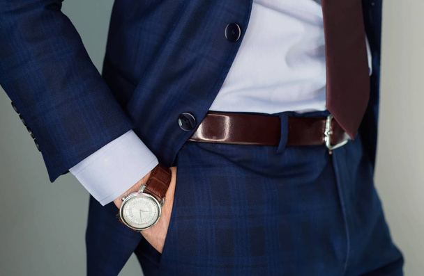 Closeup fashion image of luxury watch on wrist of man.body detail of a business man.Man's hand in blue pants pocket closeup at white background.Man wearing blue jacket and white shirt.Not isolated - Photo, image