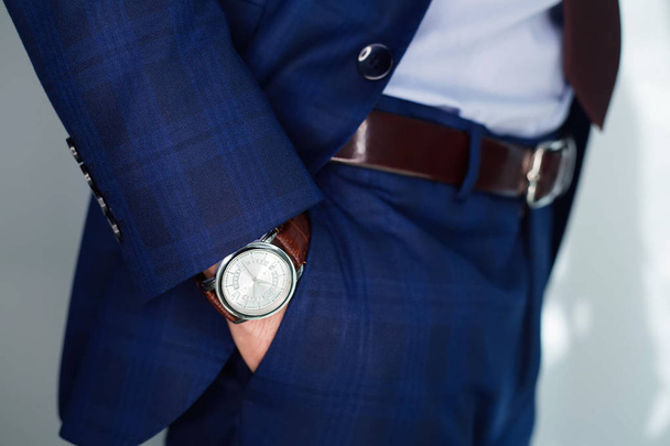 Closeup fashion image of luxury watch on wrist of man.body detail of a business man.Man's hand in blue pants pocket closeup at white background.Man wearing blue jacket and white shirt.Not isolated - Photo, image