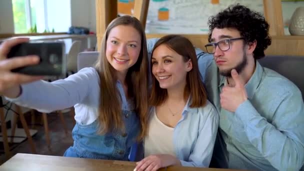 Tres amigos se sientan en un café, se divierten comunicándose y hacen selfie
 - Imágenes, Vídeo