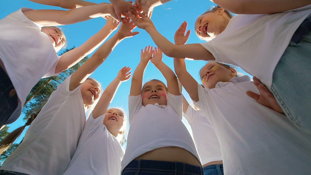 Grupy dzieci wykonuje sporty, motywacyjne pozdrowienia z ręce na boisku piłki nożnej stoczni w słoneczny dzień - Materiał filmowy, wideo