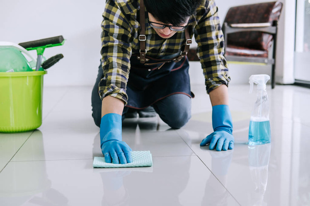Husband housekeeping and cleaning concept, Happy young man in blue rubber gloves wiping dust using a spray and a duster while cleaning on floor at home. - Foto, imagen