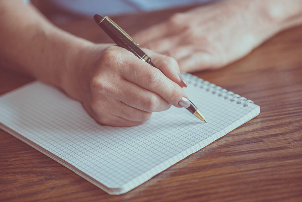 Vrouwelijke hand met pen schrijven op notebook - Foto, afbeelding