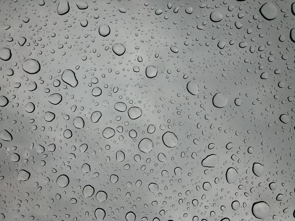 Regentropfen auf Fenstergläseroberfläche mit bewölktem Hintergrund natürliches Muster von Regentropfen isoliert auf bewölktem Hintergrund  - Foto, Bild