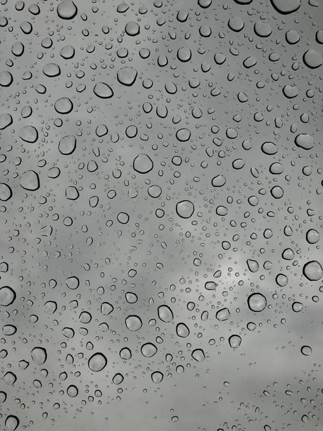 Rain drops on window glasses surface with cloudy background Natural Pattern of raindrops isolated on cloudy background  - Photo, Image
