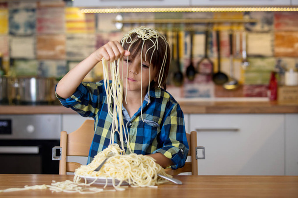 Little preschool boy, cute child, eating spaghetti for lunch and making a messat home in kitchen - Fotoğraf, Görsel