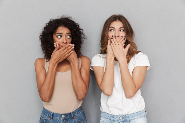 Portrait of two shocked women covering mouths isolated over gray background - Fotó, kép