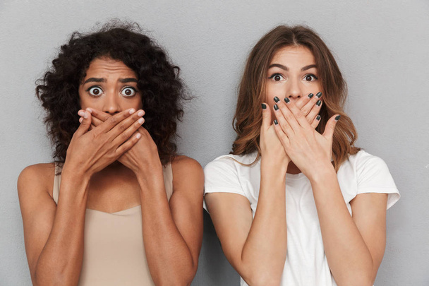Close up portrait of two shocked women covering mouths isolated over gray background - Fotografie, Obrázek