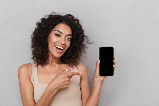 灰色の背景の上の空白の画面携帯電話での笑みを浮かべて若いアフリカ女性の人差し指の肖像画 - 写真・画像