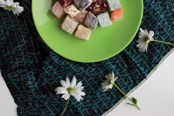 Sweets of  turkish delights and fresh camomile on green background - Photo, Image