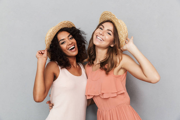 Portrait of two smiling young women dressed in summer clothes looking at camera isolated over gray background - Foto, imagen