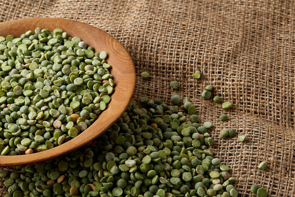 Organic green peas in a bowl on burlap tablecloth, close-up, top view, selective focus. - Fotó, kép
