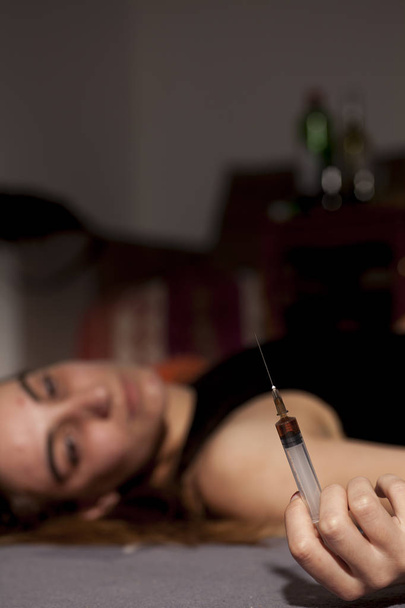 Uyuşturulmuş kız onun elinde bir şırınga yerde yatarken - Fotoğraf, Görsel