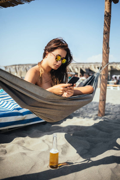 Pretty Caucasian woman lying on beach and typing on her cell phone. - Foto, Imagem