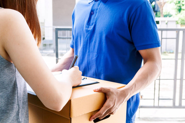 Woman putting signature in clipboard on cardboard box with delivery man  - Photo, Image
