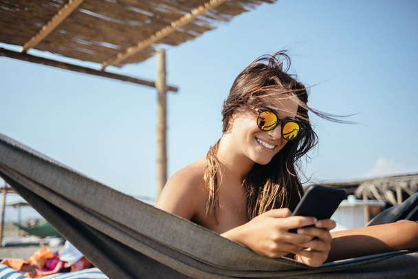 hübsche kaukasische Frau liegt am Strand und tippt auf ihrem Handy. - Foto, Bild
