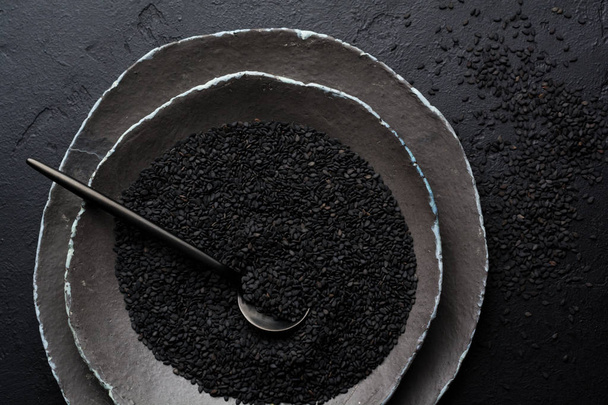 Black sesame seeds in black ceramic plates on a dark old vintage background. Rustic style. Top view. - Foto, Bild