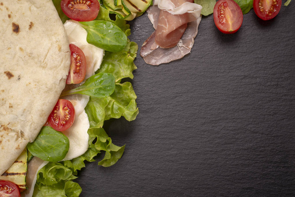 Italian piadina romagnola flatbread with lettuce, cherry tomatoes, prosciutto ham, mozzarella cheese and grilled zucchini - Φωτογραφία, εικόνα