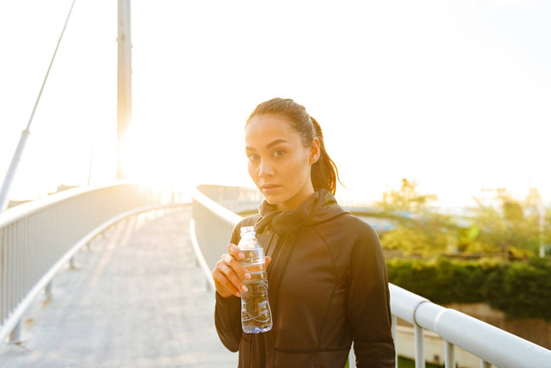 Picture of amazing beautiful young asian sports woman drinking water outdoors. - Foto, Imagem