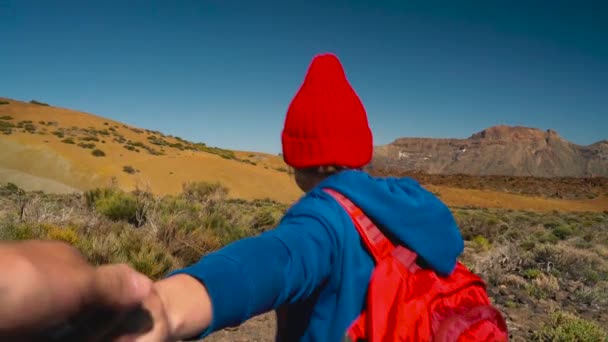 Sígueme - mujer joven feliz en sombrero rojo con mochila tirando de los chicos de la mano. Mano a mano a pie lanzan el Parque Nacional del Teide, Tenerife, Islas Canarias, España
. - Metraje, vídeo