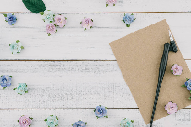 leere braune Karte und schräger Stift dekorieren mit blauen Papierblumen und grünen Blättern auf weißem Holzhintergrund mit Kopierraum - Foto, Bild