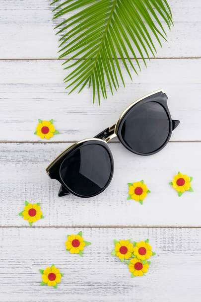 Солнечные очки украшают листья папоротника и цветы из желтой бумаги на фоне белого дерева
 - Фото, изображение