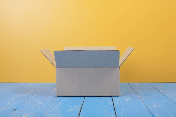 Porto- und Verpackungsservice - offene Paketfront auf blauem Holz und gelbem Wandhintergrund. - Foto, Bild