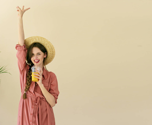s úsměvem mladá žena s kloboukem v létě drží šťávy na béžové pozadí - Fotografie, Obrázek