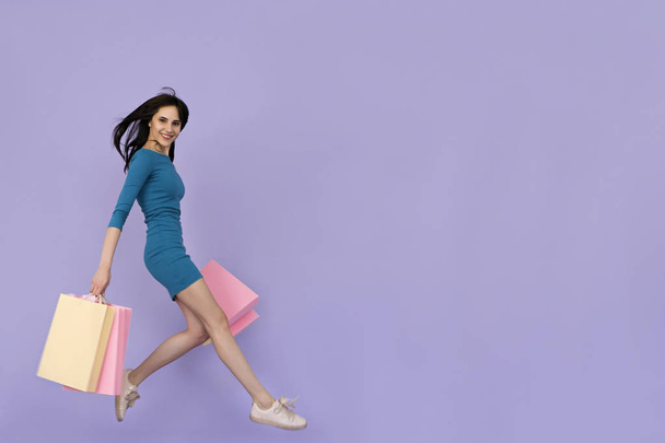 krásná mladá žena, skákání s nákupní tašky na fialové pozadí - Fotografie, Obrázek
