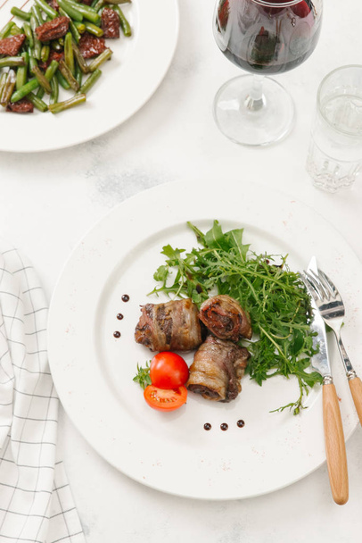 Мясорулоны со свежей рукколой и помидорами на белой тарелке
 - Фото, изображение