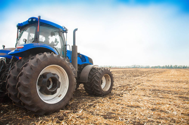 Синій трактор на тлі порожнього поля і прозорого блакитного неба
 - Фото, зображення