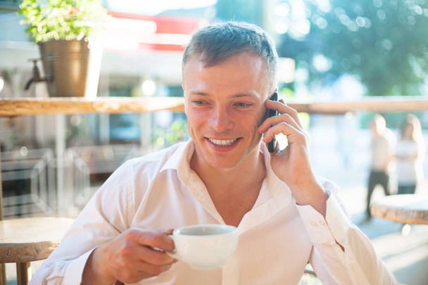 Young man drinking coffee in cafe and using phone. Business people outdoors portrait. - Foto, immagini