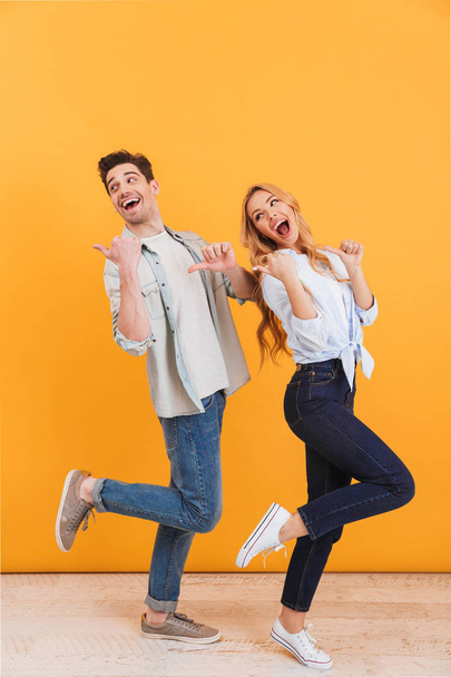 Full length photo of cheerful man and woman lookind back while pointing fingers at copyspace isolated over yellow background - Фото, зображення