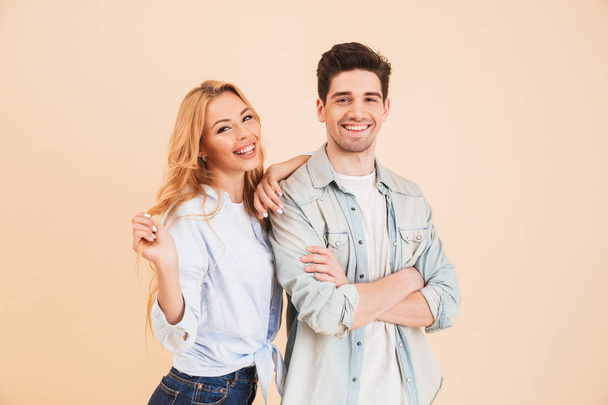 Portrait of young caucasian people man and woman in basic clothing posing together at camera with happy smile isolated over beige background - Фото, изображение