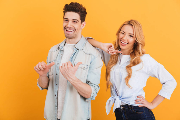 Photo of two young people in basic clothing smiling and pointing finger aside at copyspace isolated over yellow background - Valokuva, kuva